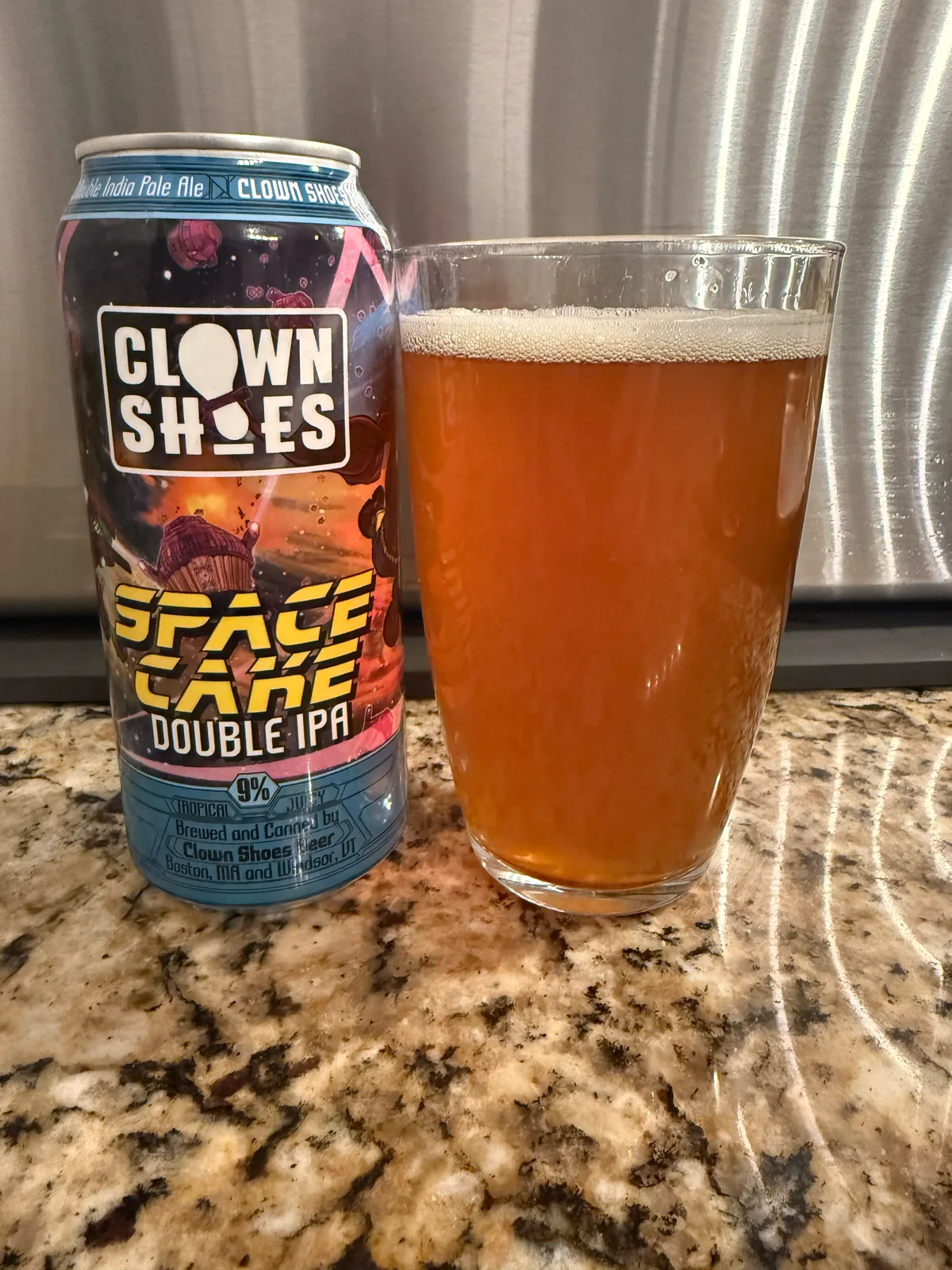 Clown Shoes Space Cake Double IPA can beside a poured hazy orange pint on a granite counter